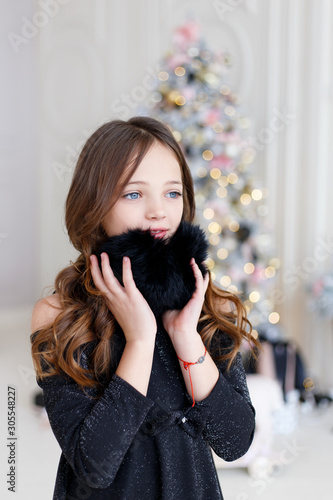  Little Girl in a Fur Headphones.  Merry Christmas and Happy New Year.  Beautiful  girl posing near the christmas tree. Christmas celebration.