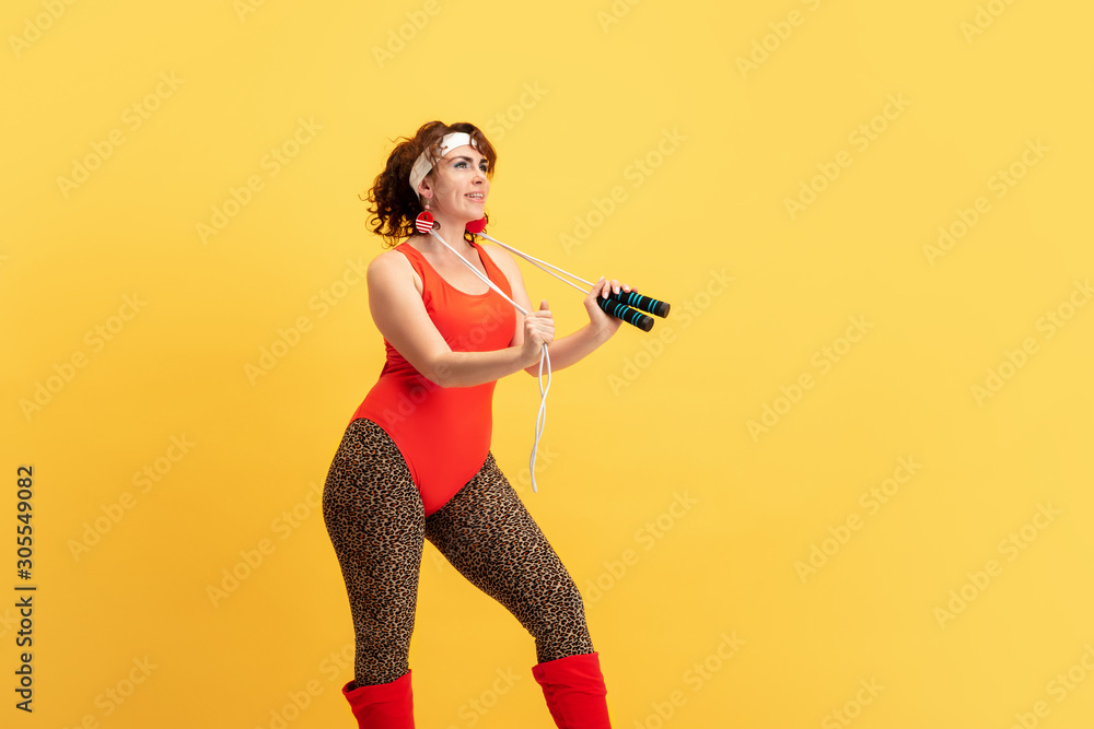 Young caucasian plus size female model's training on yellow background. Copyspace. Concept of sport, healthy lifestyle, body positive, fashion, style. Stylish woman practicing with jump rope. Young caucasian plus size female model's training on yellow background. Copyspace. Concept of sport, healthy lifestyle, body positive, fashion, style. Stylish woman practicing with jump rope.