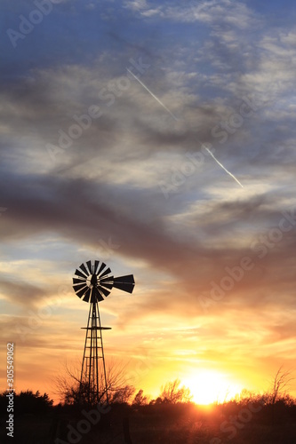 windmill at sunset with tree's and a colorful sky.