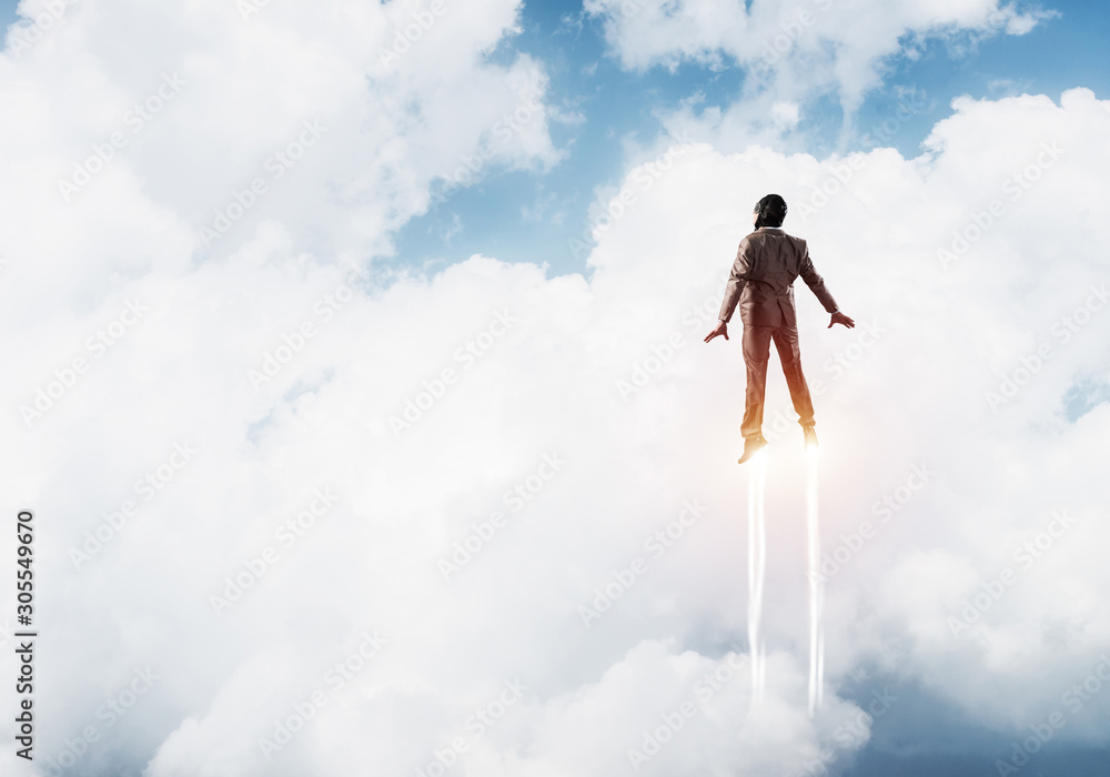 Businessman in suit and aviator hat flying in sky