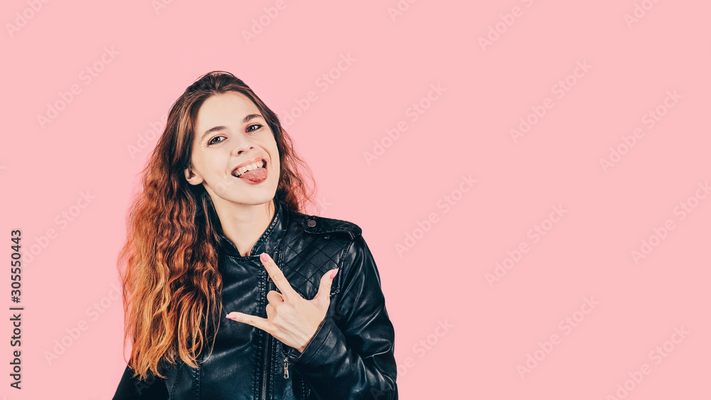 Attractive caucasian girl sticking tongue out and showing rock gesture isolated on pink background. Positive young woman. Copy space, 16:9 Attractive caucasian girl sticking tongue out and showing rock gesture isolated on pink background. Positive young woman. Copy space, 16:9