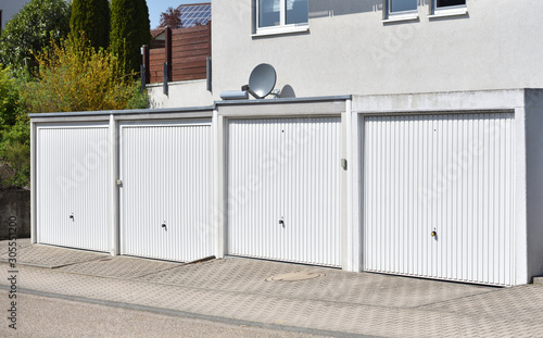 A row and four white automatic gates to a garage in a European city. Garages for four cars