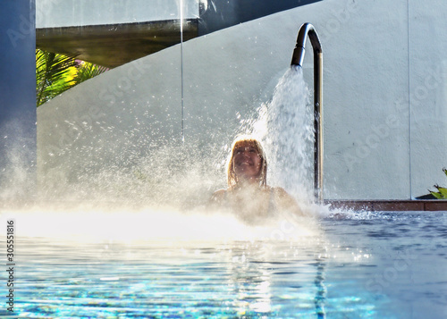   A blonde woman is standing under a strong jet of water © AkimaFutura