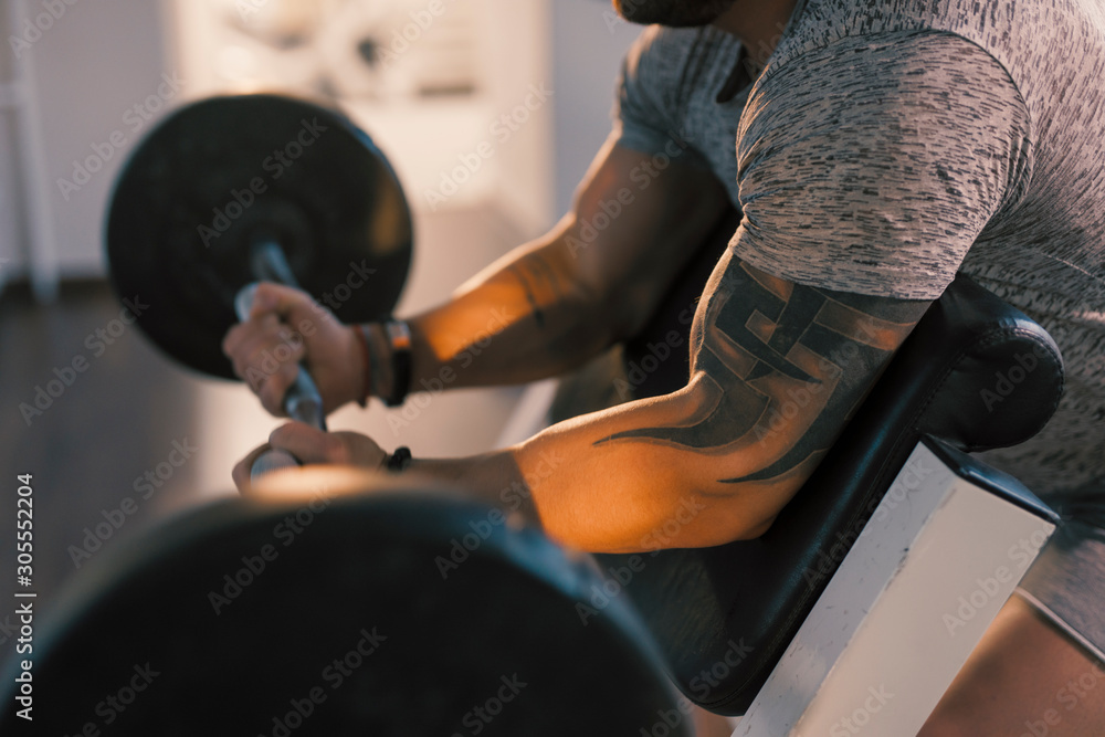 Cropped photo of the male hands lifting barbell in a gym on EZ bar preacher curl, biceps exercise