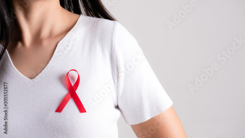 Closeup of red badge ribbon on woman chest to support AIDS Day. Healthcare, medicine and AIDS awareness concept.