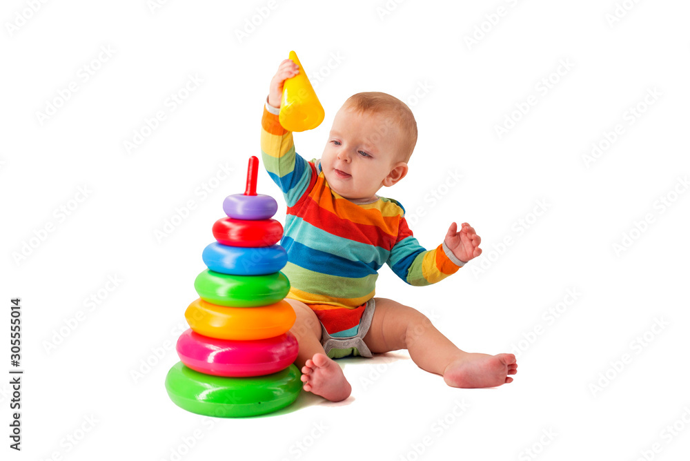 Charming cute baby in overalls plays with a colored plastic pyramid sitting on a white background. A child collects a colored pyramid Charming cute baby in overalls plays with a colored plastic pyramid sitting on a white background. A child collects a colored pyramid