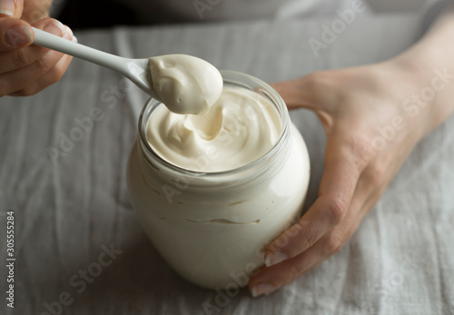 Woman holds in her hands a glass jar of mayonnaise or sour cream with a spoon. photo