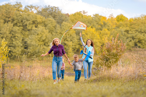 Happy non traditional family of two young mother and their kids launch a kite on nature at sunset