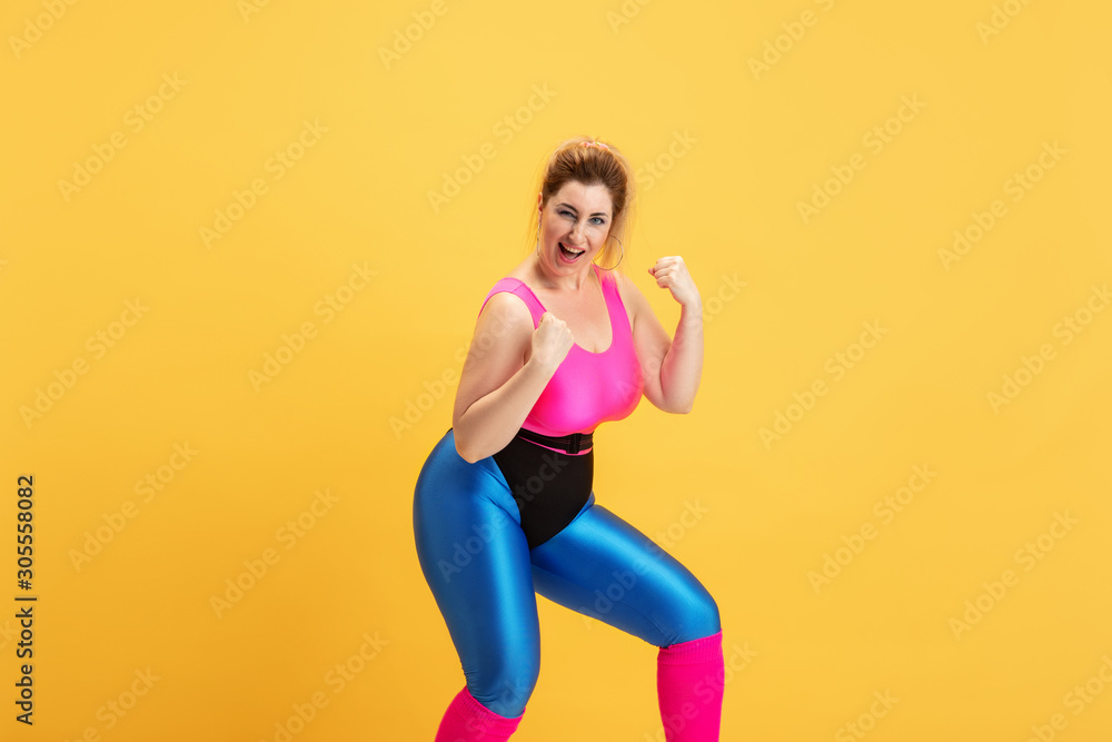 Young caucasian plus size female model's training on yellow background. Copyspace. Concept of sport, healthy lifestyle, body positive, fashion, style. Stylish woman posing like superhero, girl power. Young caucasian plus size female model's training on yellow background. Copyspace. Concept of sport, healthy lifestyle, body positive, fashion, style. Stylish woman posing like superhero, girl power.