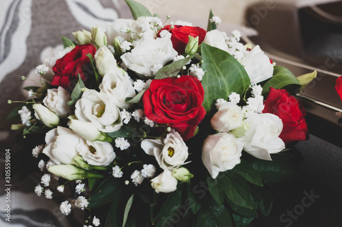 close up of bridal bouqet with red, white roses and green leaves at home