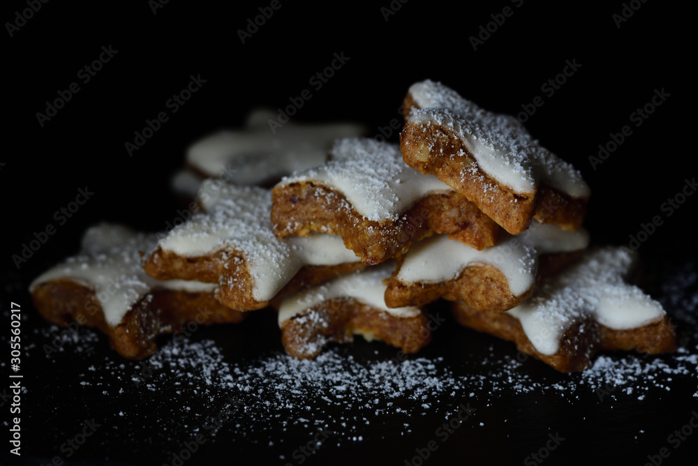 Fresh biscuits in the form of stars with white frosting and powdered sugar against dark background
