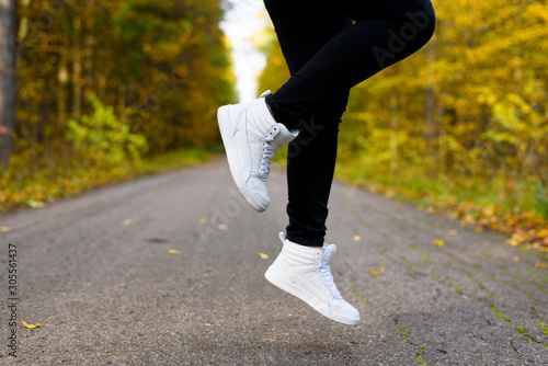 Low angle view of woman legs in white stylish sneakers over ankle in air. Jumping person. Casual sporty shoes. Concept of trends in footwear for autumn and spring.