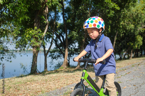 Cute little Asian 3 - 4 years old toddler boy child wearing safety helmet learning to ride first balance bike in sunny summer day, kid playing & cycling at park, Cycling with young kids concept 