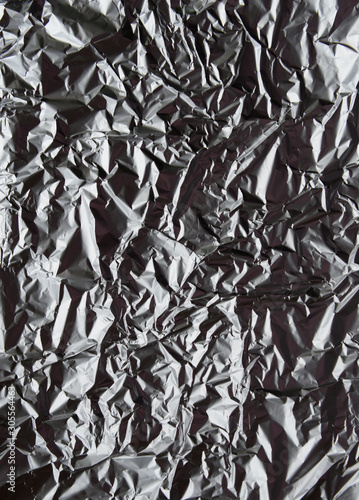 Crumpled silver aluminum foil closeup background texture. Abstract metallic paper holographic effect pattern. Vertical top view