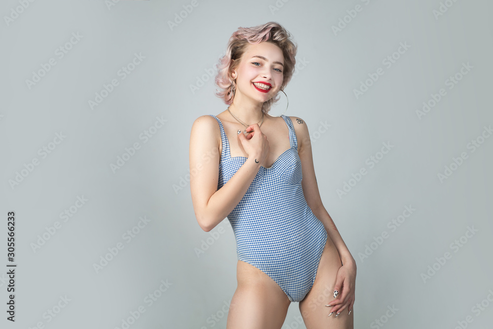 Fototapeta premium Sexy blonde woman wearing blue swimwear posing on grey background. Female sexy body. Beautiful female model posing. Portrait of sensual girl in blue swimwear. Swimwear model.