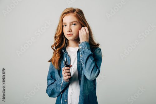 Red-haired girl listens to music in small headphones. She does not want to talk to her parents and turns on something on her smartphone