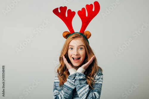 A student girl is very surprised to see such discounts on Christmas presents. A schoolgirl with freckles in a blue sweater is shocked with happiness by surprise. Isolate on a white background.