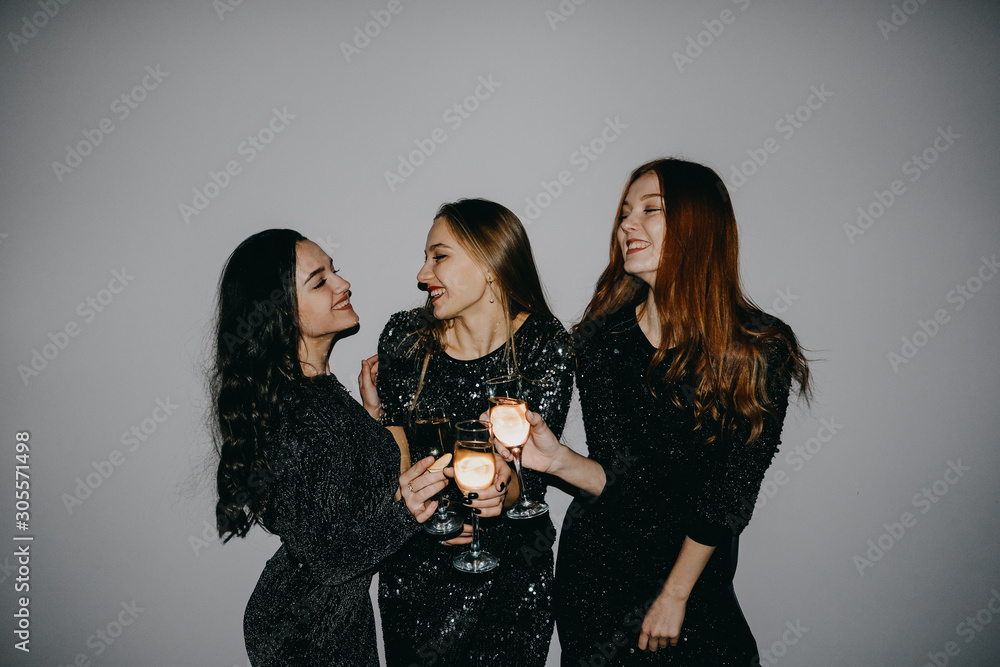 New year celebration party in the club. Three beautiful women in black sparklers night fashion dress singing and dancing with bottle glass of alcohol. Blonde, brunette and redhead celebrate birthday.