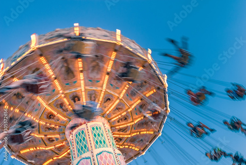 Amusement park motion blurred riders on retro vintage tilting swing against clear blue sky.