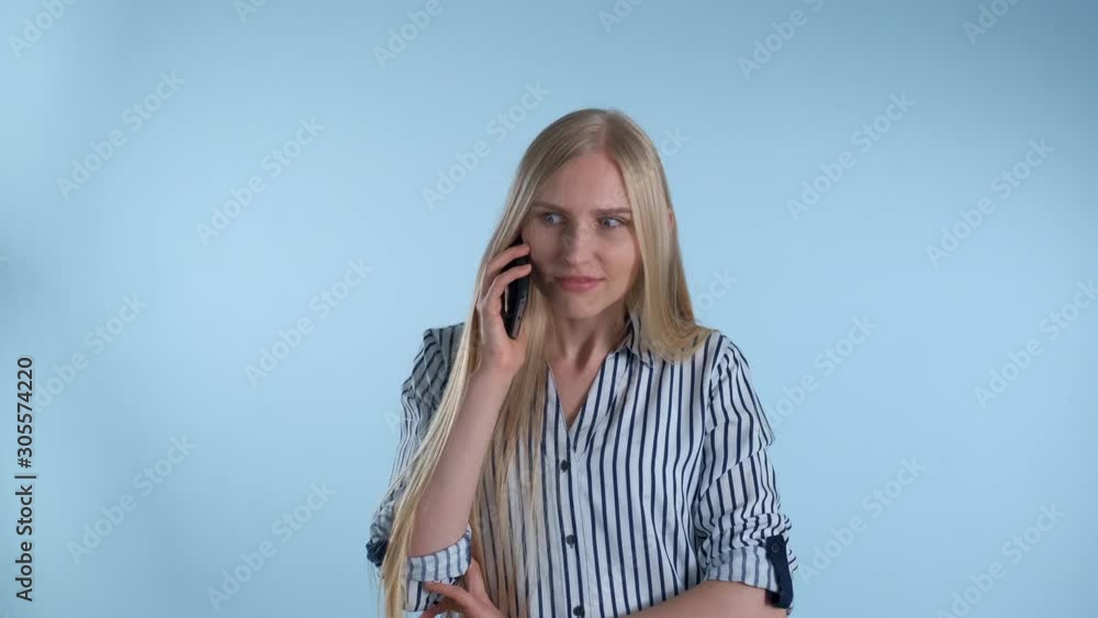 Pleasant-looking young lady speaking with somebody by smartphone on blue background. She got amazing news from friend. Pleasant-looking young lady speaking with somebody by smartphone on blue background. She got amazing news from friend.