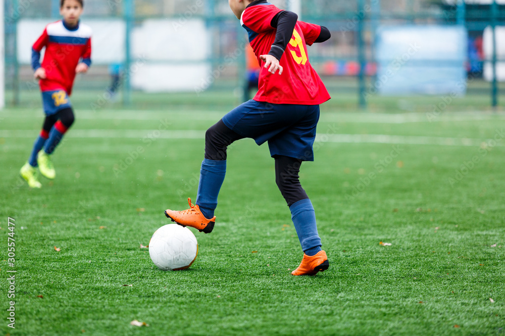 Boys in red and blue sportswear plays football on field, dribbles ball. Young soccer players with ball on green grass. Training, football, active lifestyle for kids concept Boys in red and blue sportswear plays football on field, dribbles ball. Young soccer players with ball on green grass. Training, football, active lifestyle for kids concept