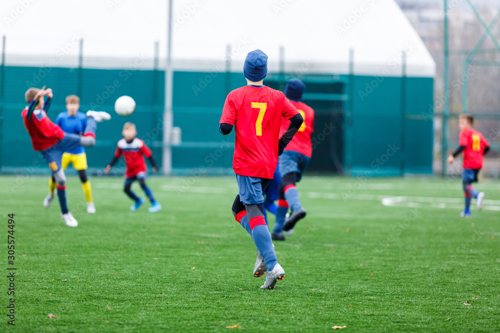 Boys in red and blue sportswear plays football on field, dribbles ball. Young soccer players with ball on green grass. Training, football, active lifestyle for kids concept Boys in red and blue sportswear plays football on field, dribbles ball. Young soccer players with ball on green grass. Training, football, active lifestyle for kids concept