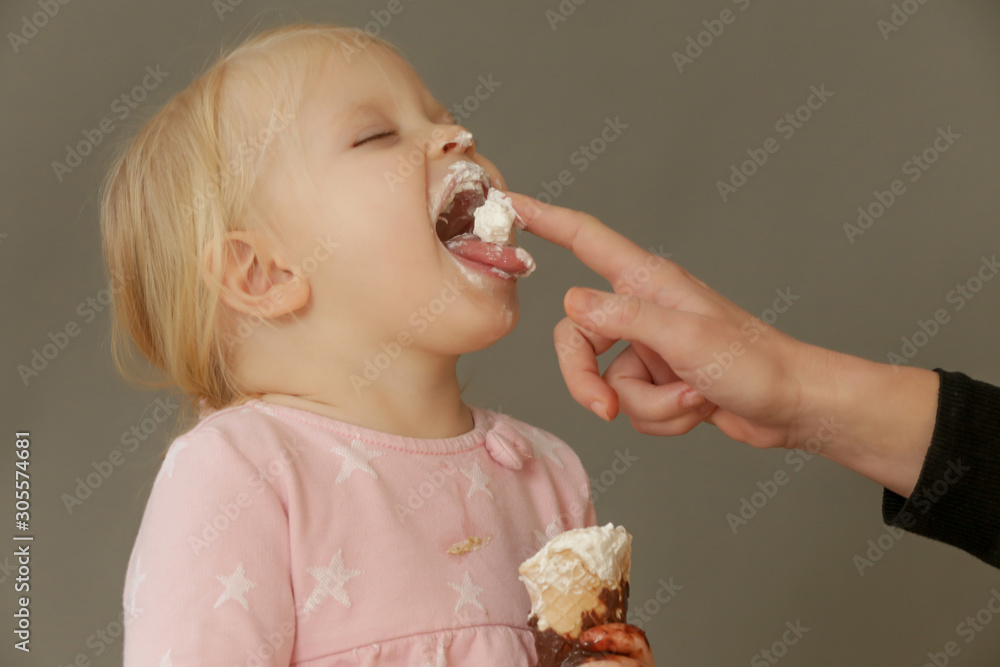 Studio shot of two years old girl eating cone ice cream. Sugar and