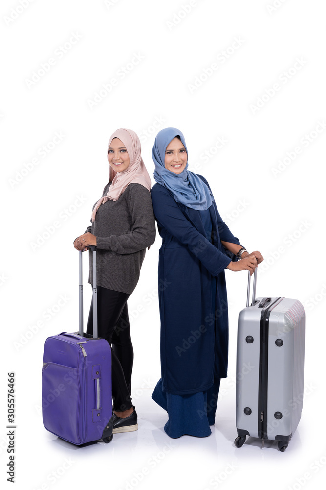 Young veiled woman and her mother holding suitcase with smile when looking the camera Young veiled woman and her mother holding suitcase with smile when looking the camera