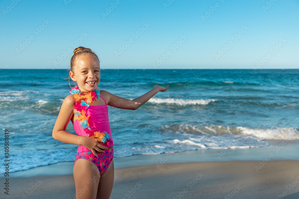 A laughing cute little girl in a colorful pink swimsuit with hawaiian ...