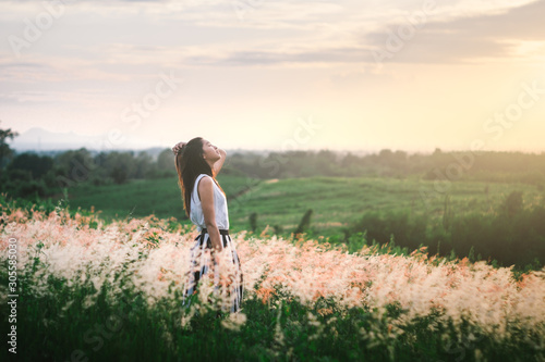 Trendy girl in stylish summer dress feeling free in the field with flowers in sunshine.