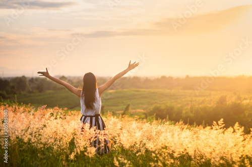 Trendy girl in stylish summer dress feeling free in the field with flowers in sunshine.
