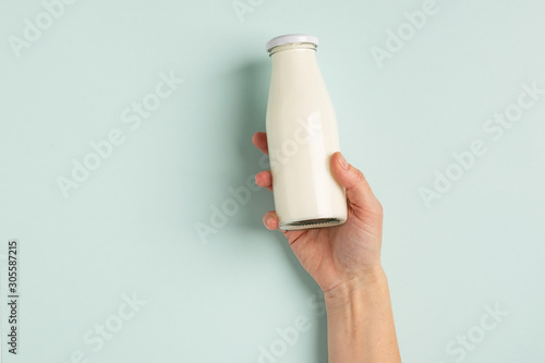 Female hand holds milk or white milk drink in a glass bottle on white background. Healthy eating concept. Flat layout .