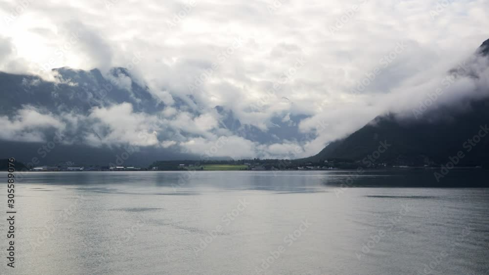 View to the beautiful Norwegian village with the traditional red and white houses at the fjord. Mountains covered with clouds on a rainy day. View to the beautiful Norwegian village with the traditional red and white houses at the fjord. Mountains covered with clouds on a rainy day.