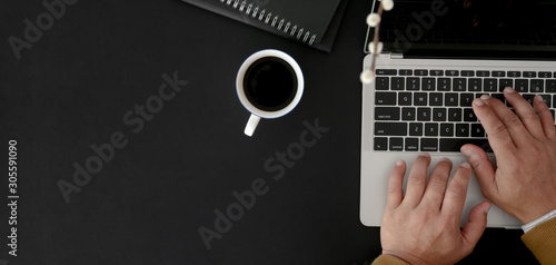 Top view of businessman typing on laptop computer in dark modern workplace on black table