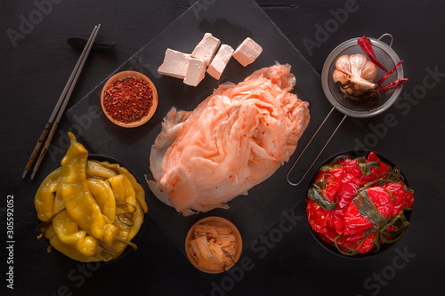 Fermented kimchi cabbage, red and yellow hot peppers with tofu on a black table - traditional Korean food. Top view