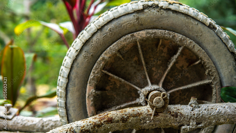 Close up view of tire of an old rusty 3-wheeled wheelbarrow with plant nature background.