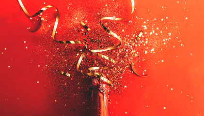 Bottle of red champagne with gold glitter, sparkles, confetti on red background, top view. New year background. flat lay.