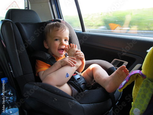 Smiling little boy in baby car seat travel by car and try to eat his finger