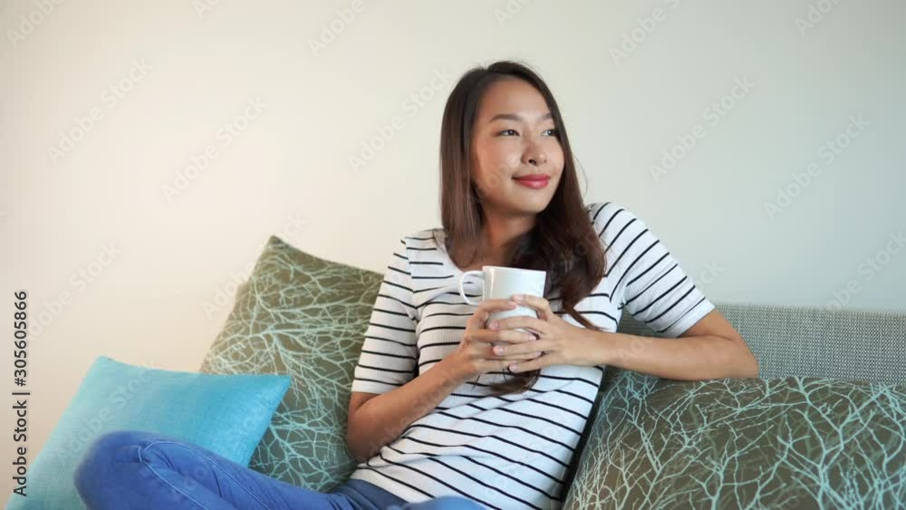 attractive brunette woman drinking from a white mug wearing a striped white shirt and blue jeans leans back on a couch with green and blue pillows and smiling contently attractive brunette woman drinking from a white mug wearing a striped white shirt and blue jeans leans back on a couch with green and blue pillows and smiling contently