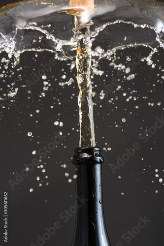 Cork flies out of a champagne bottle with a stream and splashes of wine