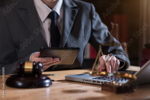 Justice and law concept.Male judge in a courtroom the gavel, working with digital tablet computer on wood table.