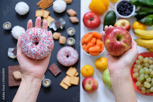 Healthy and unhealthy food concept, apple and donut in hand. Top view photo