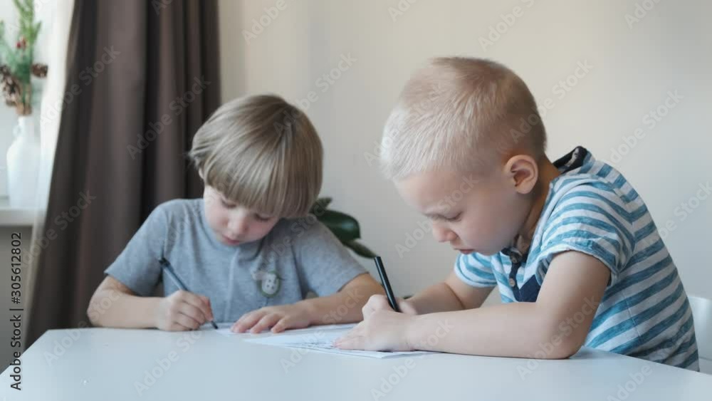Two little boys sitting at the table at home and drawing Two little boys sitting at the table at home and drawing