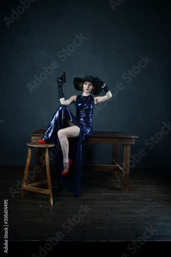 girl in a blue evening dress and in a black hat on a gray background with a gun