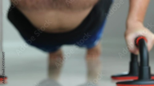 Slowmo and extreeme close up of a young shirtless man working out on the floor of his house. Low angle shot focusing on the face and push up bars. photo