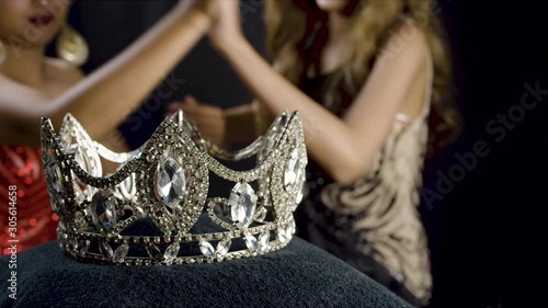Two beauty pageant contestants fight, catfight, over a jewel crown which is in close up focus in the foreground with the struggle for the prize in the background photo
