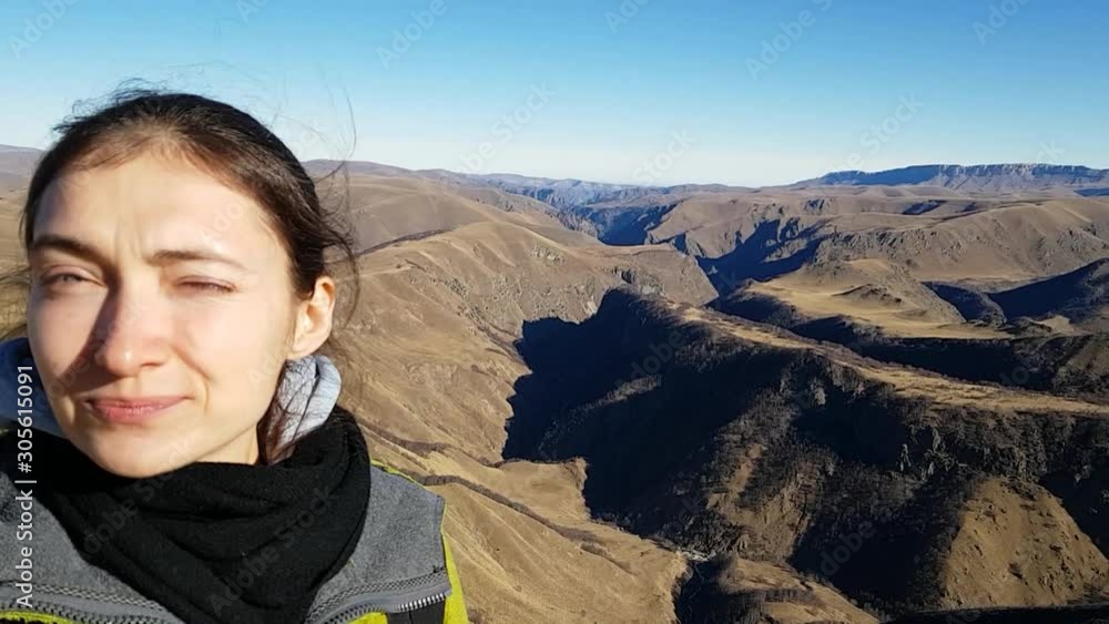 A beautiful young brunette woman squints in the bright autumn sun. A backpacker takes a selfie and winks into her cell phone. Hiking in the mountains A beautiful young brunette woman squints in the bright autumn sun. A backpacker takes a selfie and winks into her cell phone. Hiking in the mountains