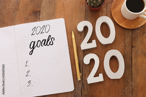 Business concept of top view 2020 goals list with notebook, cup of coffee over wooden desk