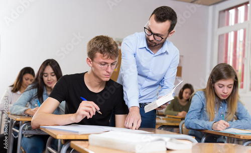 Young boy is writing test and teacher is explaining about questions