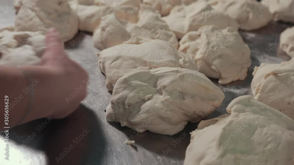 Closeup of pieces of dough lay on stainless steel working table. One hand with wedding ring, bracelet takes elastic white dough. Single piece falls down before chef. Closeup of pieces of dough lay on stainless steel working table. One hand with wedding ring, bracelet takes elastic white dough. Single piece falls down before chef.